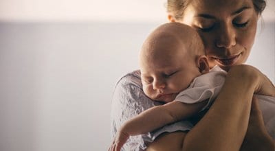 mother holding newborn baby over her shoulder